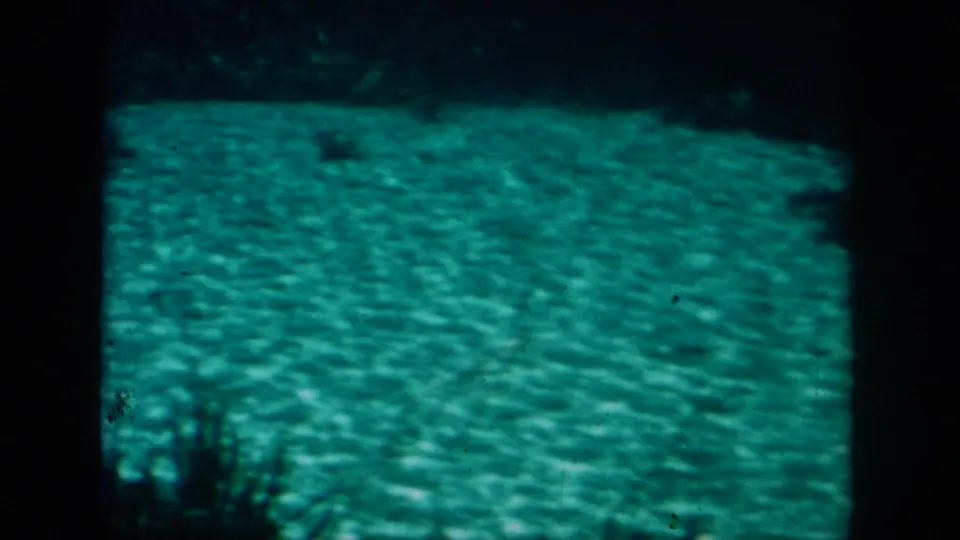 1958 home-movie frame showing another murky underwater view, with green water, bottom texture, and dark film-edge framing.