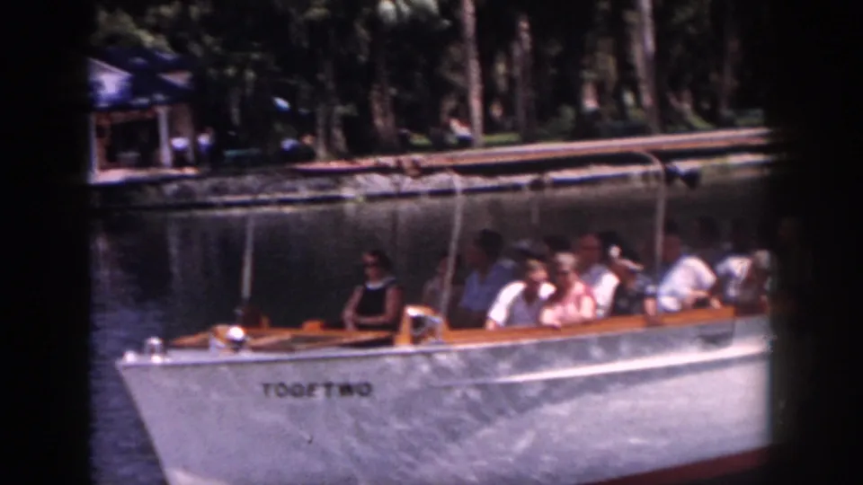 1958 New Orleans frame showing a white tour boat named TOOETWO carrying seated passengers beside trees and calm water.