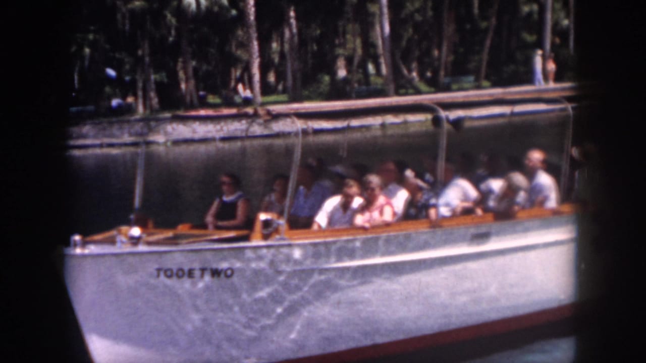 1958 New Orleans home-movie frame showing tourists seated aboard a white boat on a calm canal-like waterway.