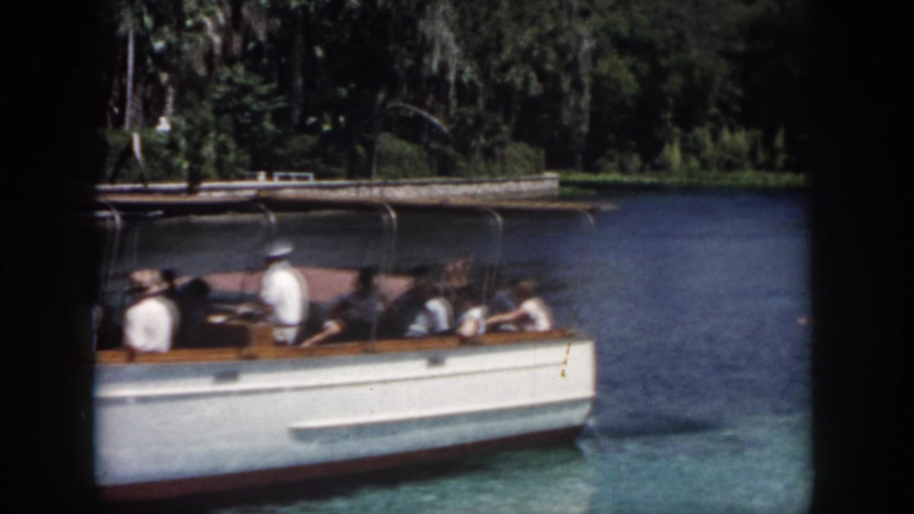 1958 New Orleans home-movie frame showing a white tour boat with seated passengers on calm water near trees.