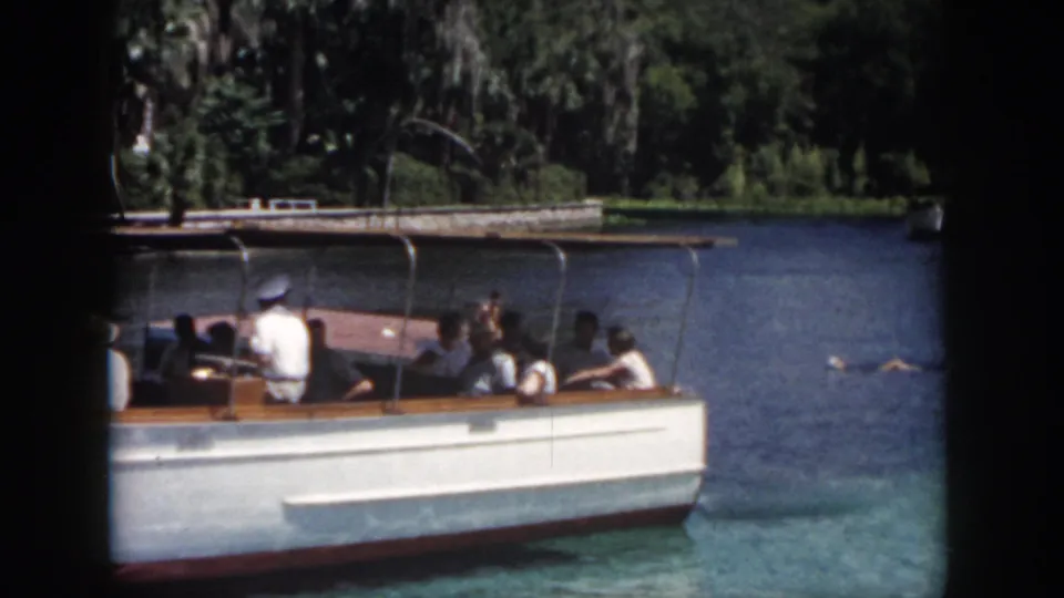 1958 New Orleans frame with a white tour boat, seated passengers, and a swimmer visible in the water nearby.
