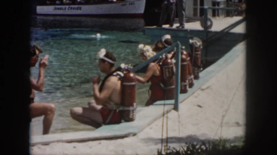 1958 New Orleans dockside frame with scuba divers, swimmers, and a background boat labeled Jungle Cruise.