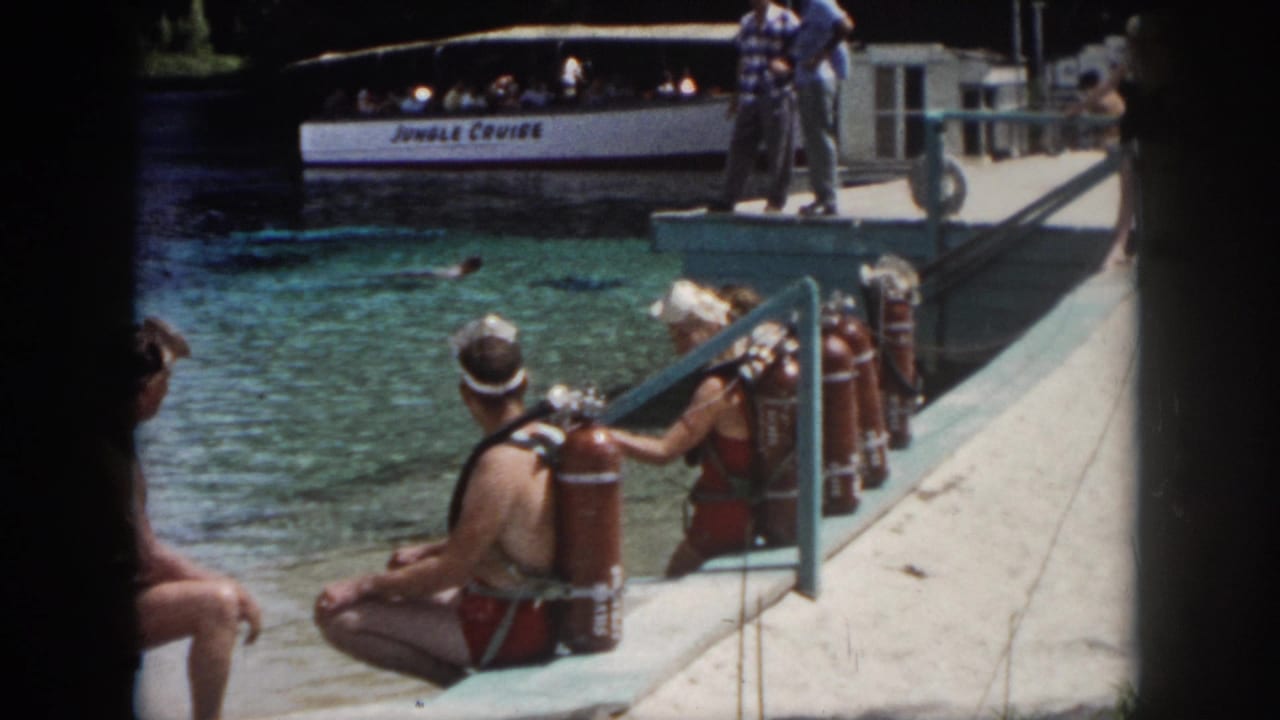 1958 New Orleans attraction footage showing scuba participants on a concrete dock, with a white Jungle Cruise boat carrying passengers behind them.