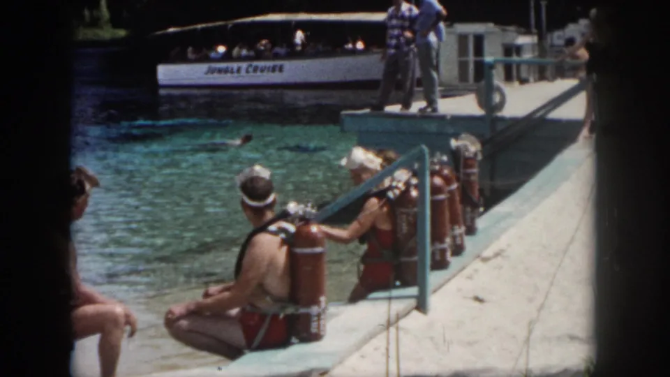 1958 New Orleans attraction footage showing scuba participants on a concrete dock, with a white Jungle Cruise boat carrying passengers behind them.