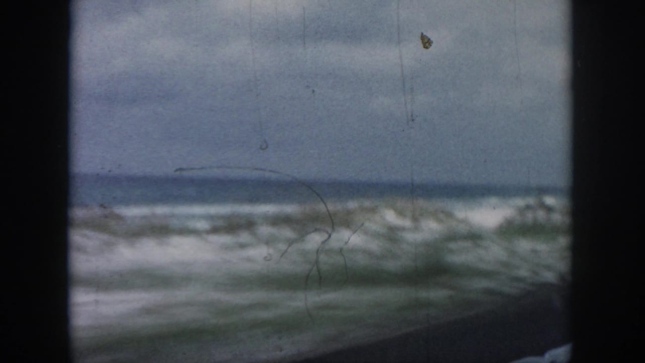 1958 8mm view near New Orleans showing rough surf, sandy dunes, and sparse grass framed by a vehicle window.