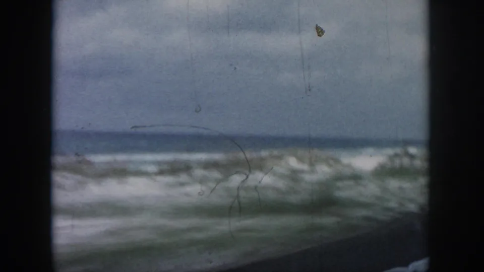 1958 8mm view near New Orleans showing rough surf, sandy dunes, and sparse grass framed by a vehicle window.