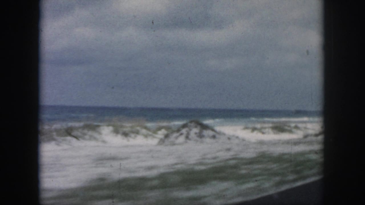 Waves break along a sandy shore beyond dark vertical window framing.