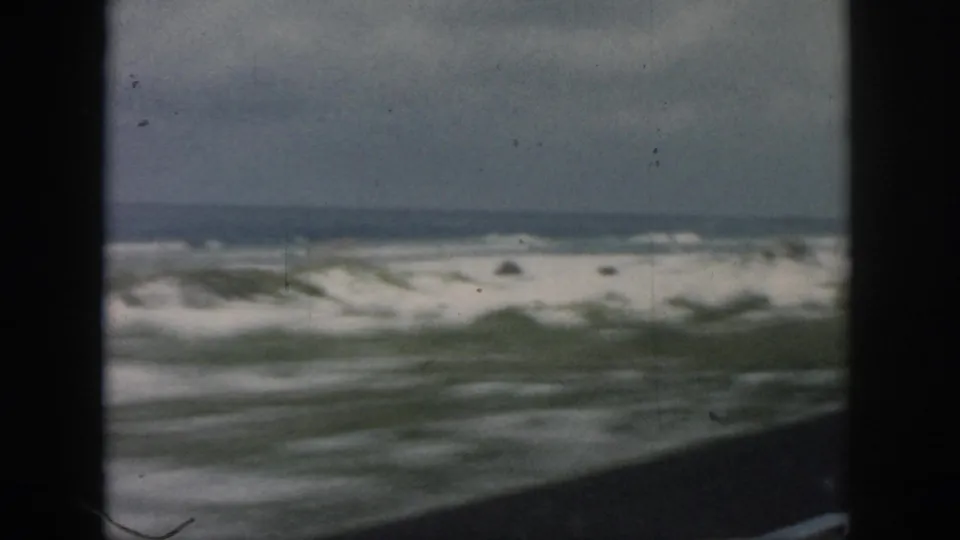 Final 1958 coastal frame shows foamy water, sandy dunes, sparse grass, and dark car-window framing near the documented New Orleans location.