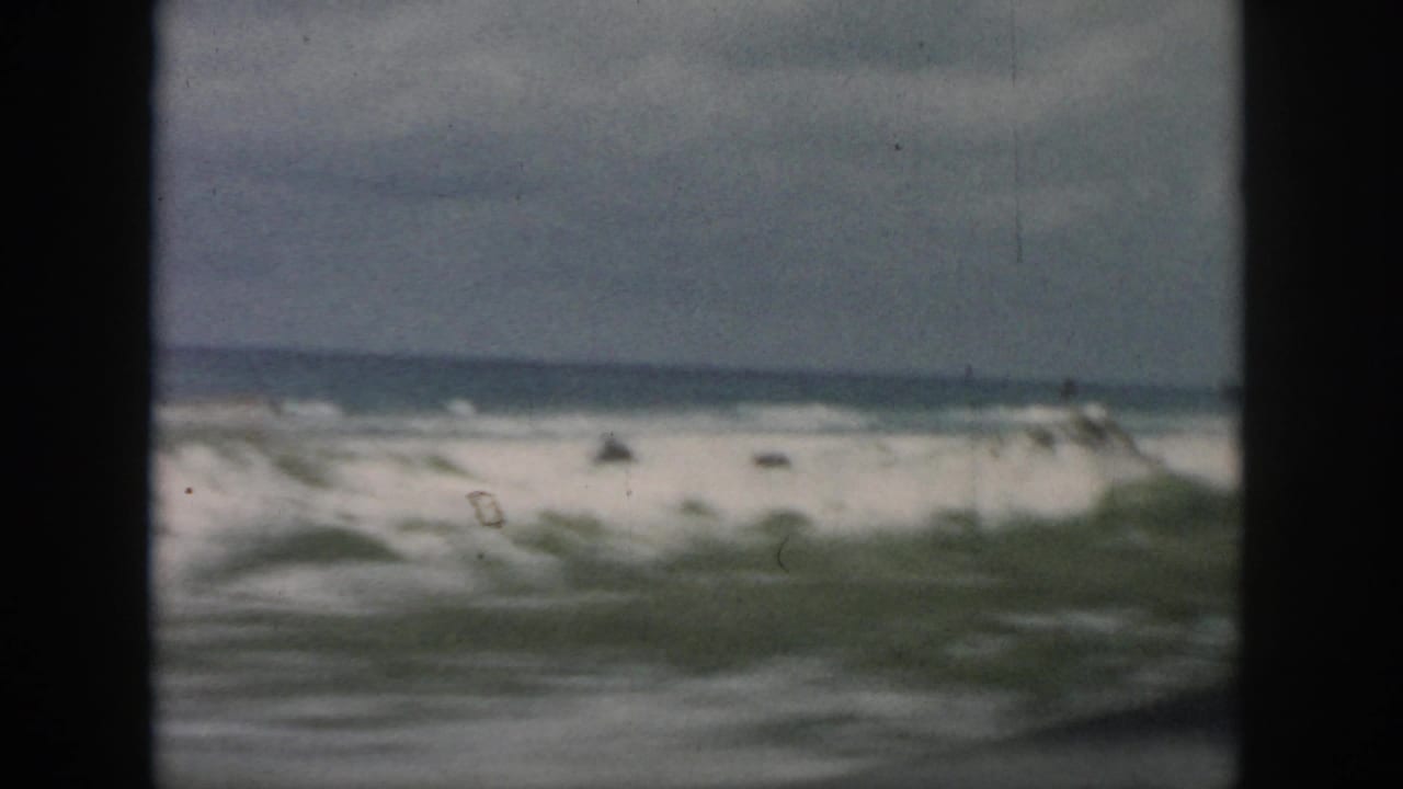 1958 8mm passenger-window view of a blurred coastal shoreline, surf, and cloudy sky near New Orleans, Louisiana.