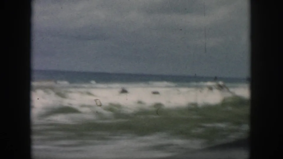 1958 8mm passenger-window view of a blurred coastal shoreline, surf, and cloudy sky near New Orleans, Louisiana.