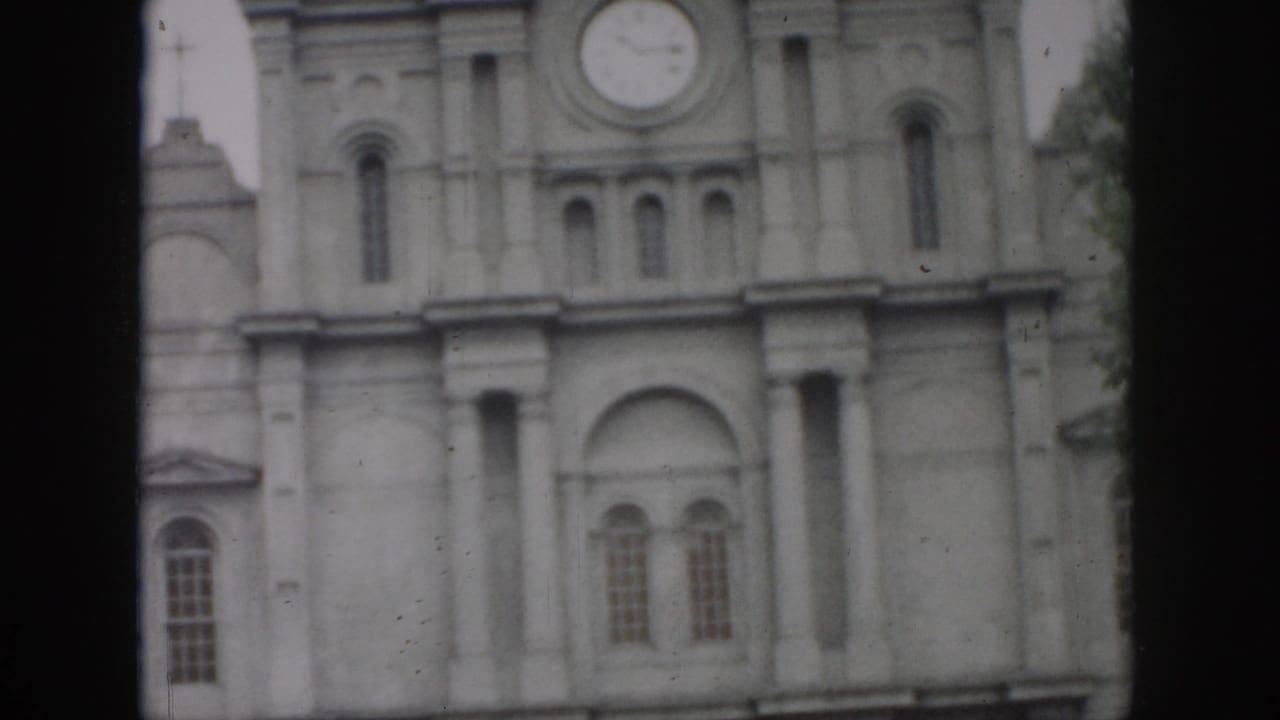 Upper facade of a stone building with a round clock and arched architectural details.