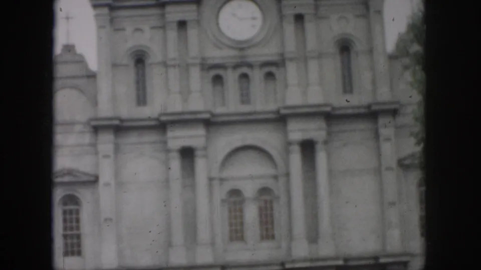 1958 New Orleans frame of a formal stone facade with a prominent circular clock, arched openings, and vertical columns.
