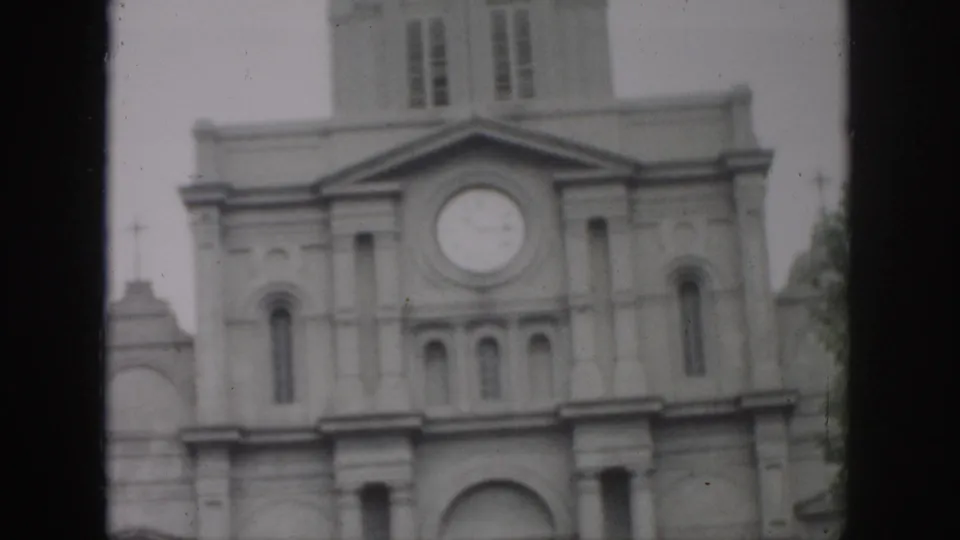 1958 New Orleans frame showing the clocked upper facade of a pale stone building, with dark 8mm borders and slight blur.