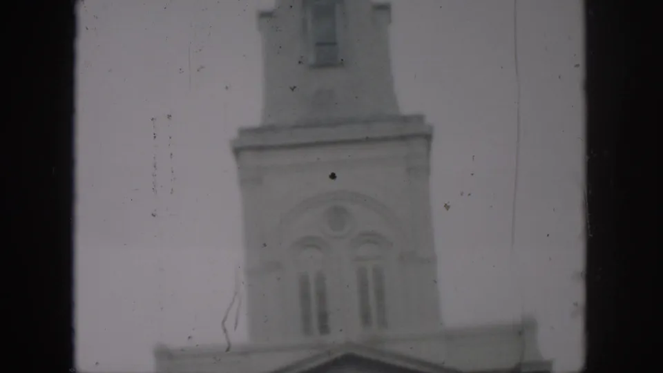 1958 New Orleans home-movie frame looking upward at the church tower, with arched windows, masonry detail, and visible film scratches.