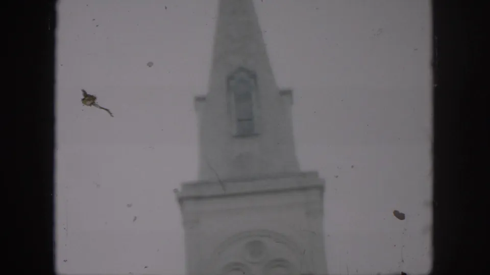 1958 New Orleans frame showing the pointed church steeple above the tower, with soft focus, dust, and a pale overcast sky.