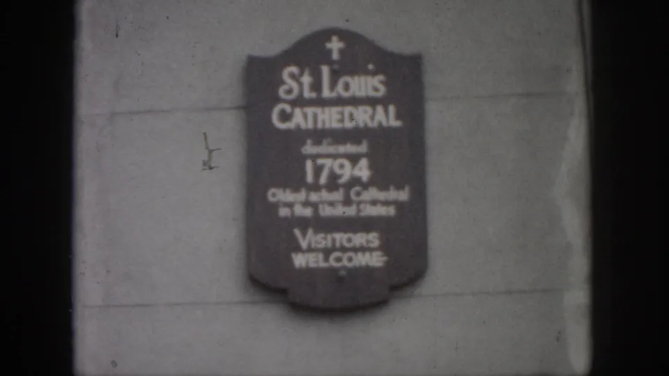 1958 New Orleans frame showing the St. Louis Cathedral visitor sign on a stone wall, including dedication and oldest cathedral text.