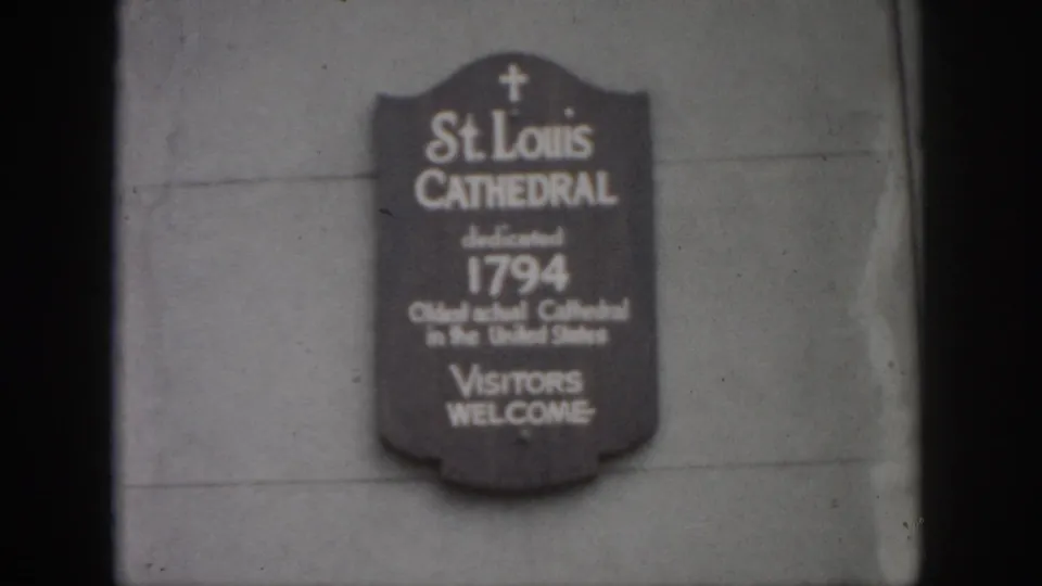 1958 New Orleans home-movie frame showing a St. Louis Cathedral plaque mounted on a stone wall, softly focused and grainy.