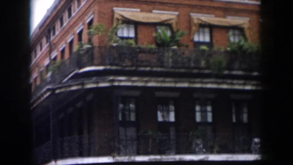 1958 New Orleans home-movie view of a brick facade near St. Louis Cathedral, with balcony ironwork, plants, windows, and awnings.