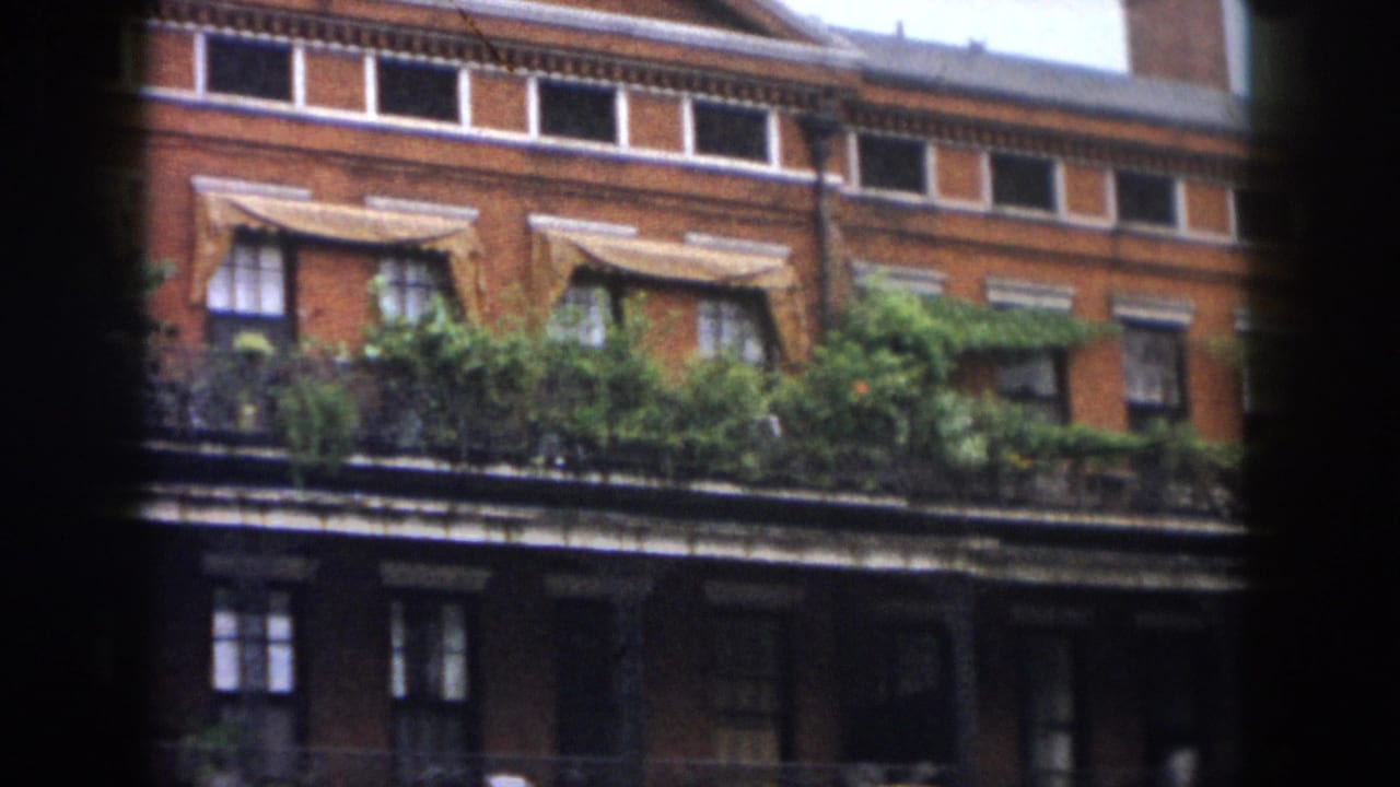 Long brick building with awnings, narrow upper windows, balcony greenery, and dark center obstruction.