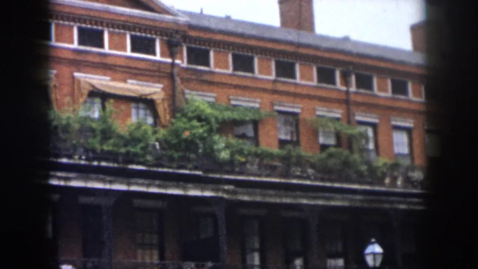1958 New Orleans frame with brick windows, balcony greenery, wrought-iron railings, and a small street lamp near the lower edge.