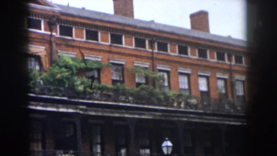 1958 New Orleans exterior showing brick walls, balcony greenery, rows of windows, awnings, chimneys, and a street lamp at lower right.