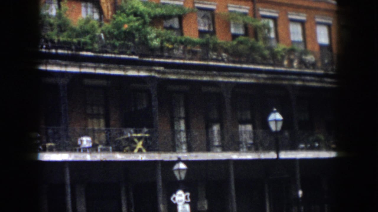 Brick facade with balcony railings, plants, street lamps, and shadowed lower level.