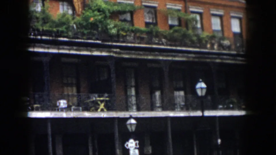 1958 New Orleans view of a brick building with balcony planting, street lamps, and a shaded lower arcade or storefront area.