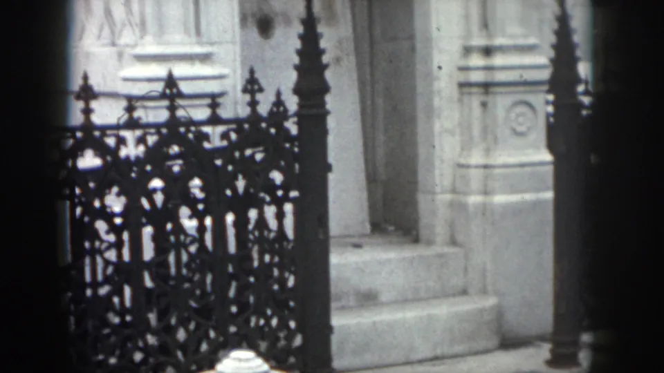 1958 New Orleans 8mm frame focusing on a decorative black iron gate, pale stone entry columns, and steps.