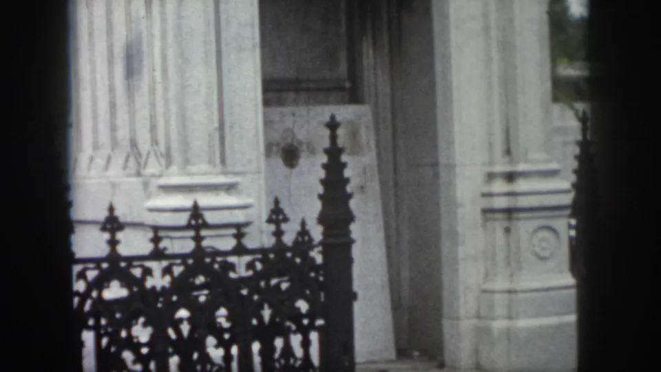 1958 New Orleans frame showing an ornate iron fence in front of pale stone columns, a doorway, and exterior architectural details.