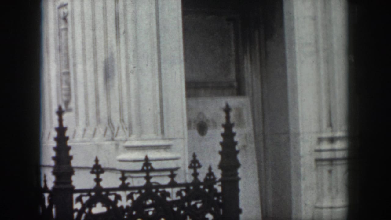 Ornate stone mausoleum entrance partly behind decorative iron fencing.