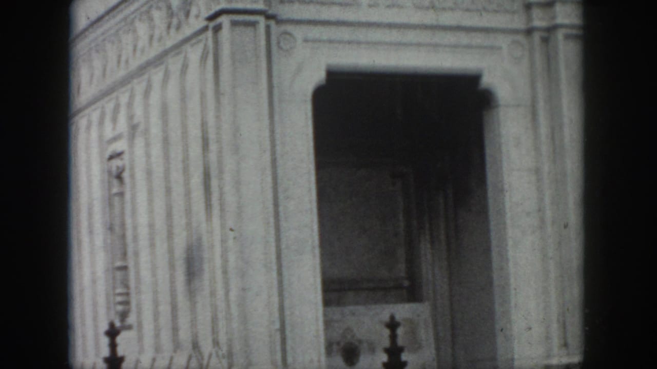 1958 New Orleans home-movie frame of a weathered stone mausoleum corner, showing a recessed arched entrance and carved architectural bands.
