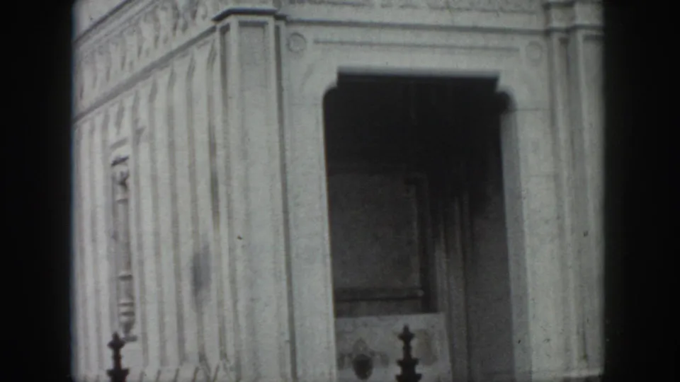 1958 New Orleans home-movie frame of a weathered stone mausoleum corner, showing a recessed arched entrance and carved architectural bands.
