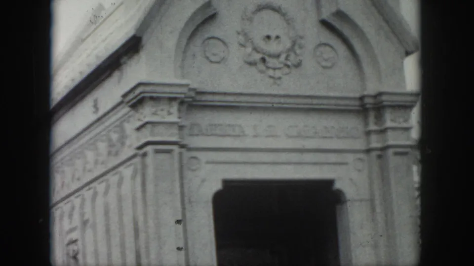1958 New Orleans frame showing the upper stone mausoleum facade, including a skull-like relief, carved trim, and a shadowed doorway below.