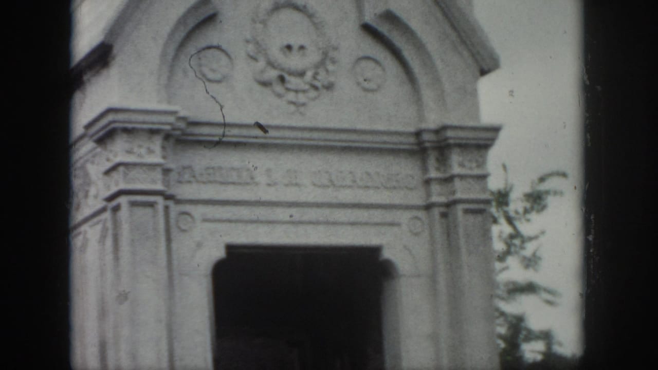 1958 New Orleans cemetery view of an ornate stone mausoleum facade with carved details and a shadowed entrance.