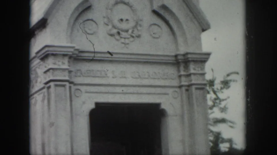 1958 New Orleans cemetery view of an ornate stone mausoleum facade with carved details and a shadowed entrance.