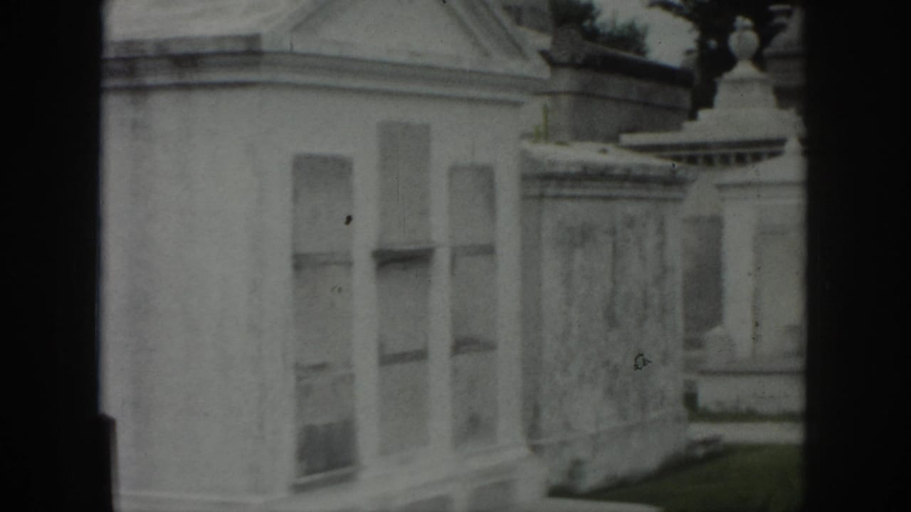 1958 New Orleans home-movie view of pale cemetery mausoleums and stone walls with soft focus and dark film edges.