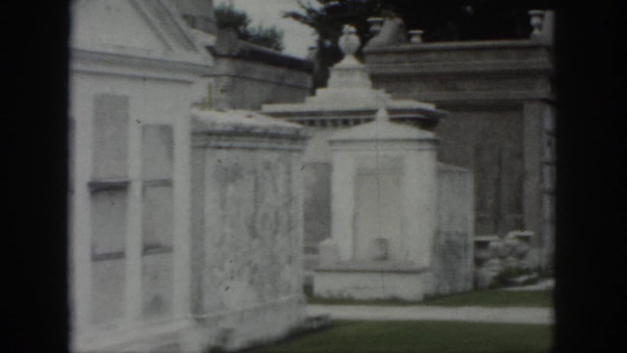 1958 New Orleans cemetery footage showing above-ground tomb walls, decorative stonework, and a narrow path.