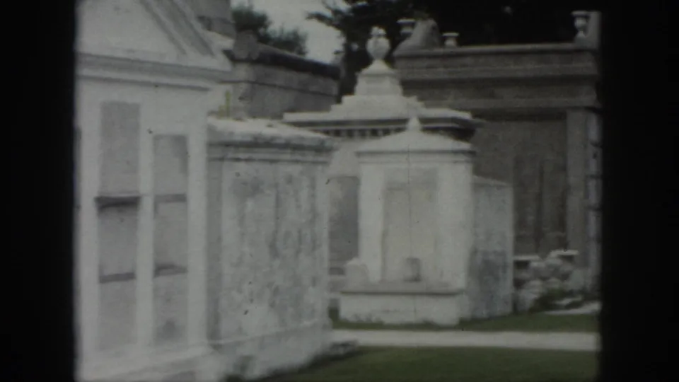 1958 New Orleans cemetery footage showing above-ground tomb walls, decorative stonework, and a narrow path.