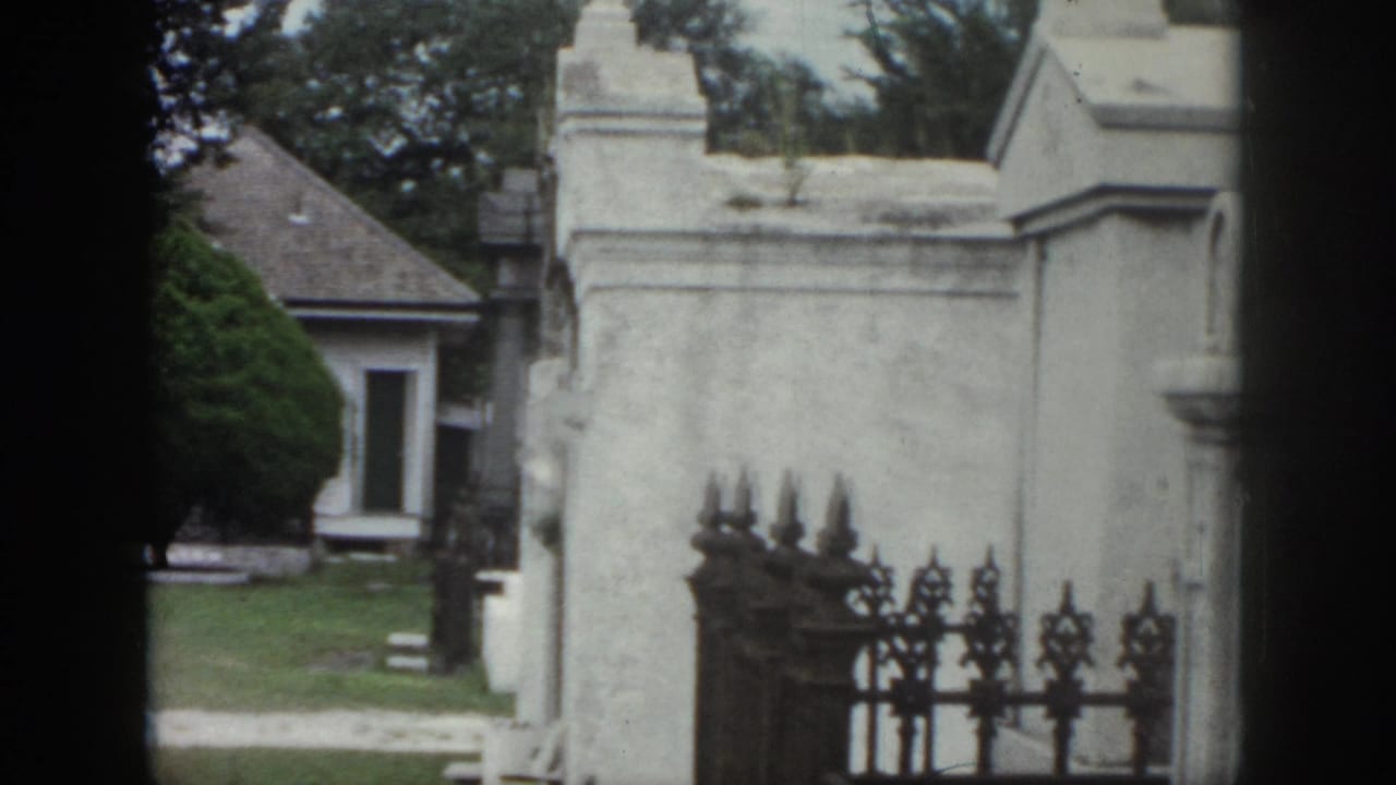 Stone cemetery pillars and an iron gate frame a view of tombs and lawn.