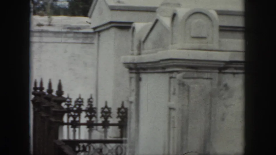New Orleans cemetery footage from 1958 showing ornate iron fencing, pale stone tombs, and weathered above-ground burial structures.