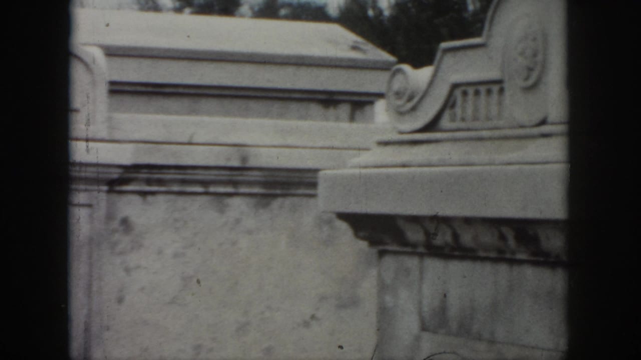 1958 New Orleans 8mm frame showing a close view of a weathered stone tomb with decorative masonry and partial engraved family text.