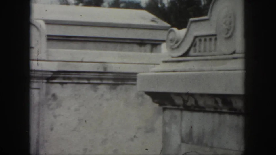 1958 New Orleans 8mm frame showing a close view of a weathered stone tomb with decorative masonry and partial engraved family text.