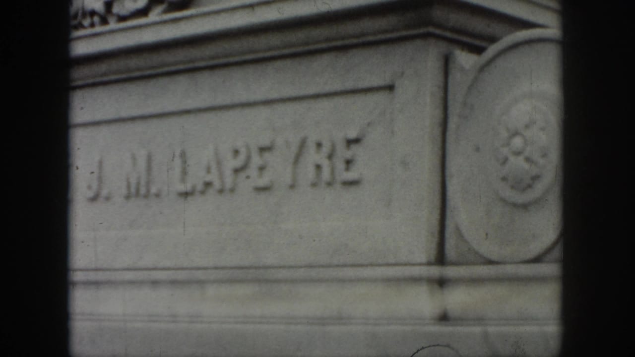 1958 New Orleans home-movie frame showing the J. M. LAPEYRE name carved into a gray stone monument, partly obscured by dark film borders.