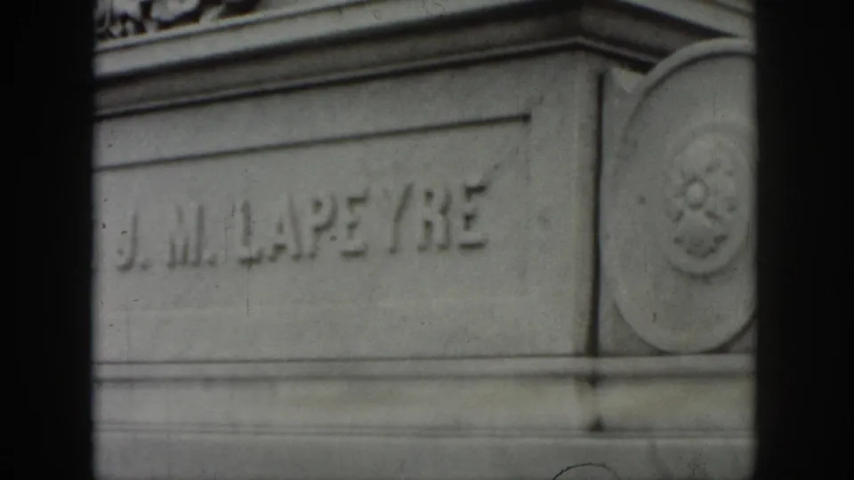 1958 New Orleans home-movie frame showing the J. M. LAPEYRE name carved into a gray stone monument, partly obscured by dark film borders.