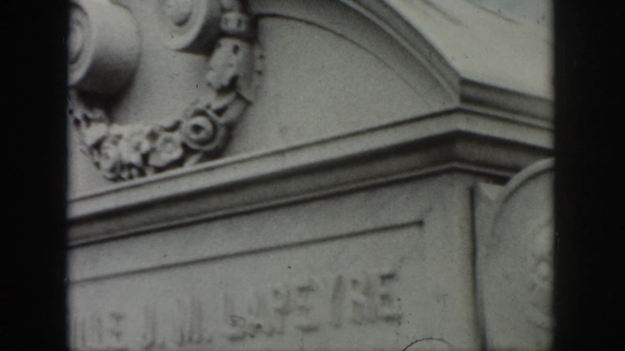Ornate upper section of a stone monument with scrollwork, floral carving, and a partial inscription below.