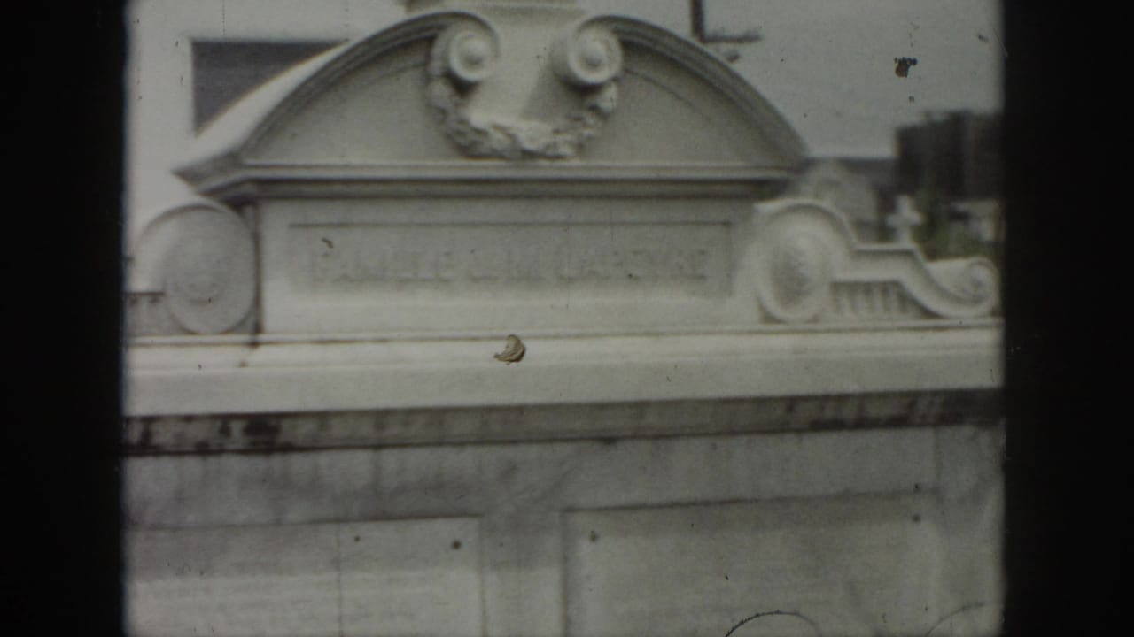 1958 New Orleans cemetery view showing an ornate above-ground tomb with carved scrollwork and a pale stone facade.