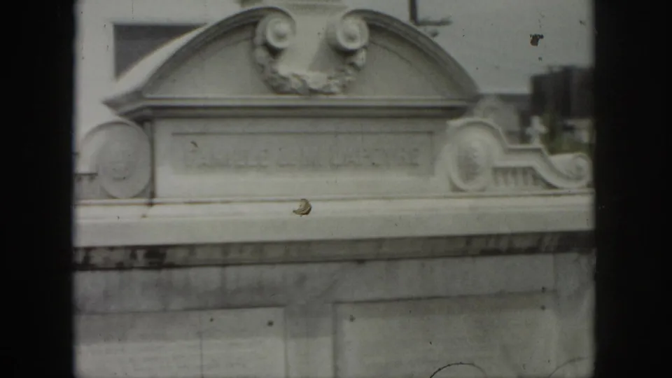 1958 New Orleans cemetery view showing an ornate above-ground tomb with carved scrollwork and a pale stone facade.