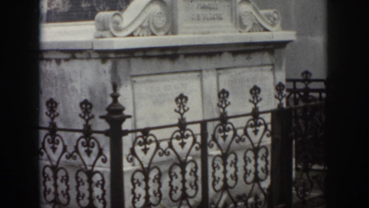 1958 New Orleans frame with a pale stone mausoleum, carved top details, inscription panels, and decorative black ironwork.