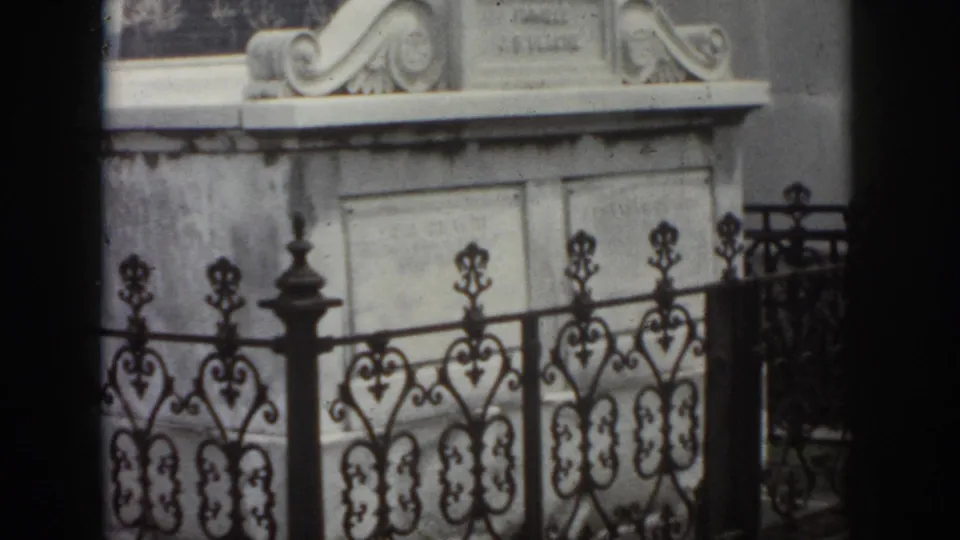 1958 New Orleans frame with a pale stone mausoleum, carved top details, inscription panels, and decorative black ironwork.