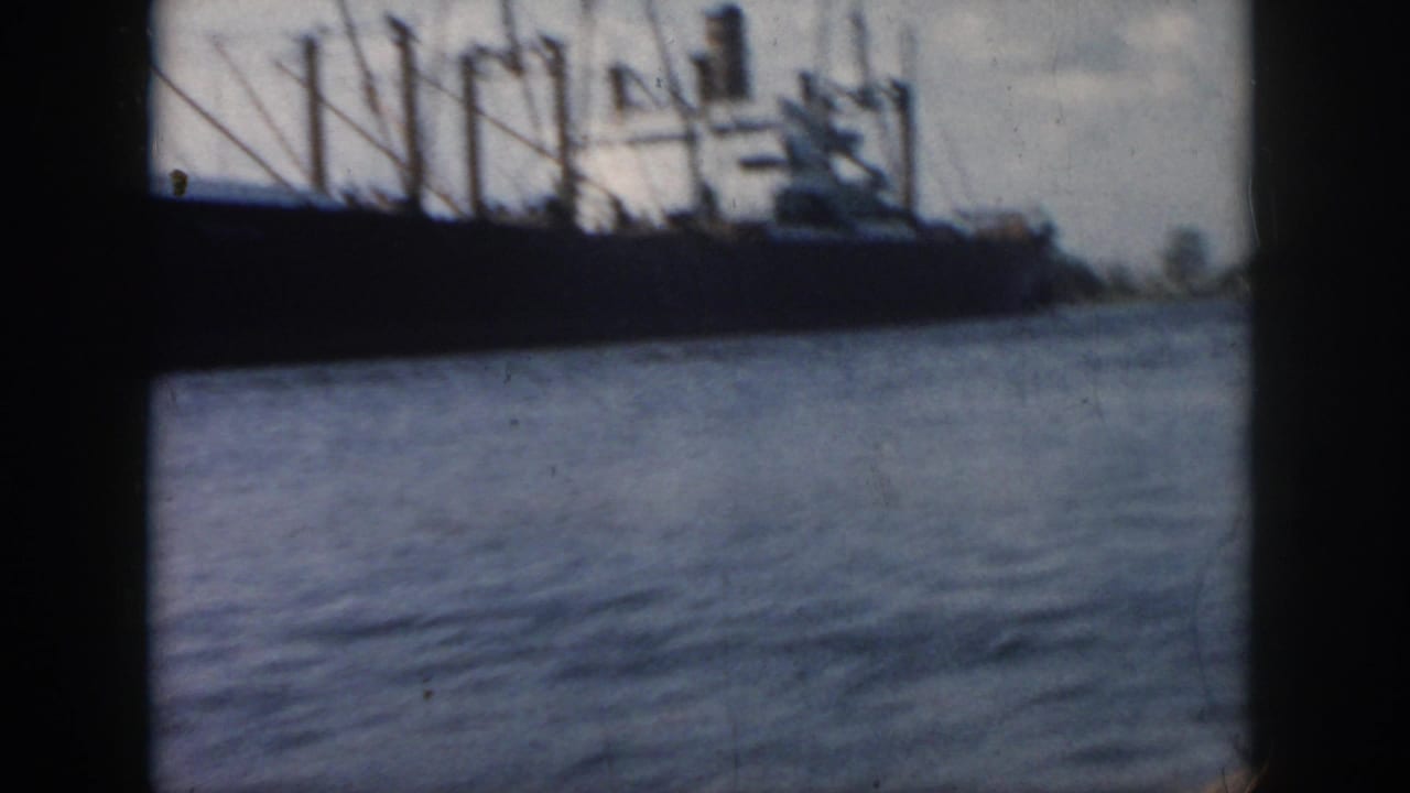 1958 New Orleans home-movie frame showing a large vessel across calm water, with rigging silhouetted against a cloudy sky.
